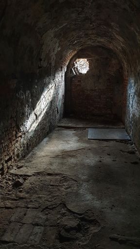 An arched dungeon with light coming from a hole on the wall