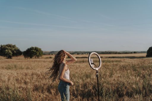 A gorgeous blonde Spanish girl flicking her hair while taking a selfie on her phone with a ring light in front of her in a field