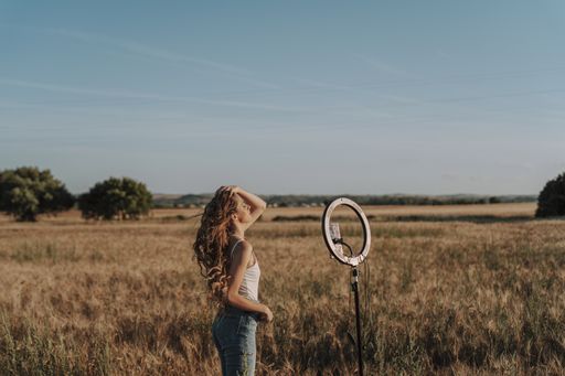 A blonde Spanish girl messing with her hair while taking a selfie with her phone on a ring light in a wheat field