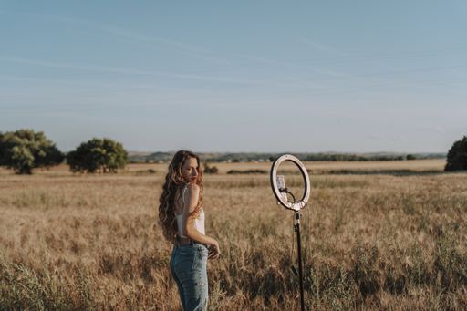 A Spanish woman taking a selfie with her phone mounted on a ring light in a wheat field