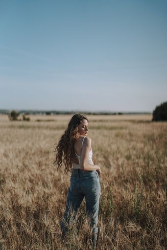 A vertical shot of a sexy Spanish woman looking over her shoulder at the ground in a sunny wheat field