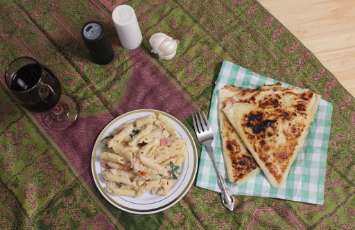 Two plates of Italian-style food with pizza and soup, accompanied by a glass of red wine, set on a wooden table against a white background