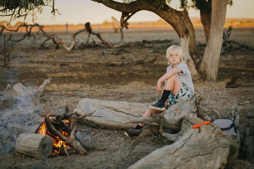 A shallow focus shot of a beautiful Australian boy sitting by the campfire