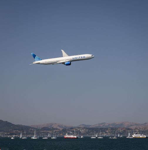 A United Airlines Boeing 777 jet flying over San Francisco bay filled with boats during a Fleet Week Airshow demonstration