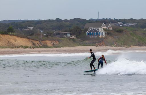 The surfers riding on the surfboards on the foamy waves of the ocean during the daytime in Chilmark