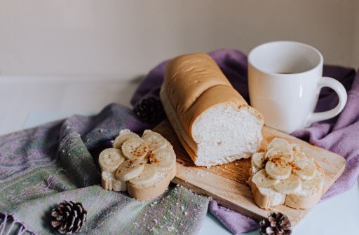A shot of a breakfast table with banana toasts, bread, and a mug of coffee under the sunlight