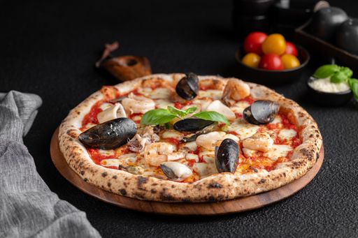 A delicious seafood pizza placed on a rustic wooden tray, accompanied by several colorful side dishes