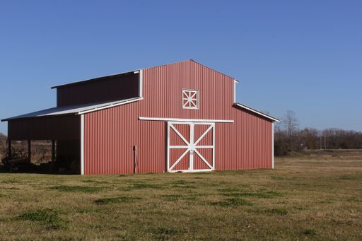 A stunning landscape featuring a large red barn situated in an open field surrounded by a fence and lush green grass