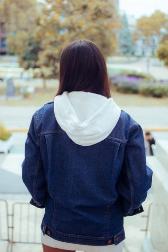 A beautiful Caucasian woman from the back wearing shorts, a jean jacket, and a hoodie