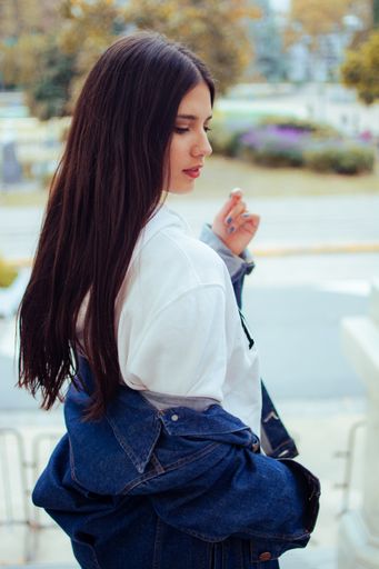 A beautiful Caucasian woman from the back wearing shorts, a jean jacket, and a hoodie