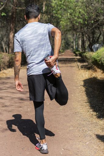 A man with a tattoo sleeve from the back wearing sportswear and stretching at the park