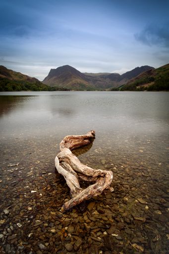 A vertical shot of a calm lake with mountains under a cloudy sky