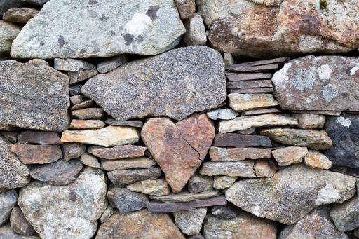 A heart-shaped stone stuck in the middle of a wall with other small and large stones
