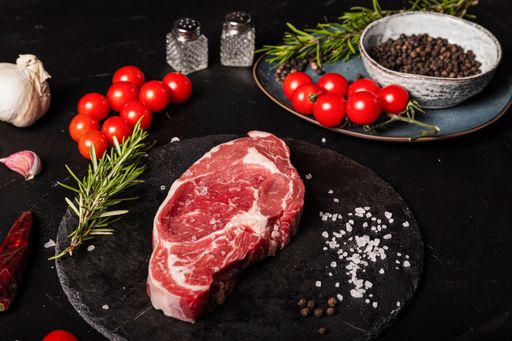 A closeup shot of raw beef Entrecote with rosemary, salt, and pepper on a round slate