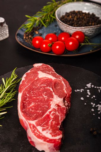 A vertical shot of raw beef Entrecote with rosemary, salt, and pepper on a round slate