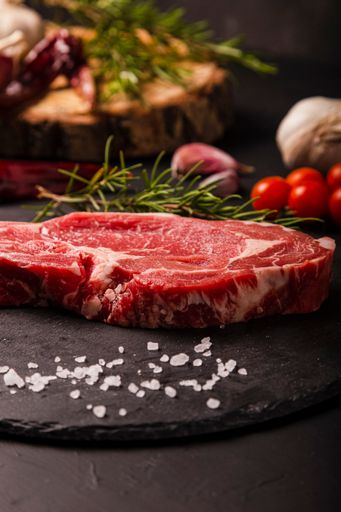 A vertical shot of raw beef Entrecote with rosemary, salt, and pepper on a round slate
