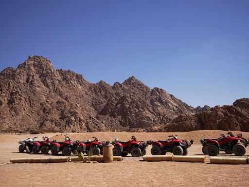 a column of red quad bikes in a dessert with large cliffs and blue sky