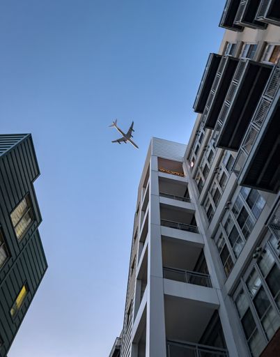 A 4 engine jet airliner flying over a building outside of Boston with a blue sky in the background