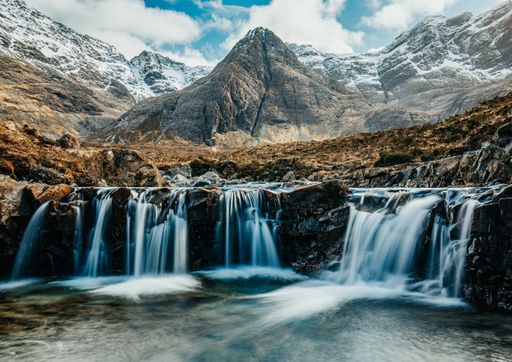 A mesmerizing view of snow-covered rocky mountains and a waterfall under a cloudy sky