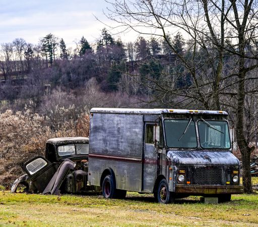 A rusted truck parked in field with stacked old cars