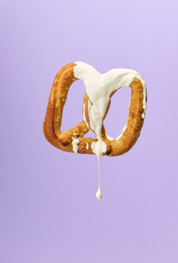 A closeup of a pretzel bathed in white chocolate on lilac background