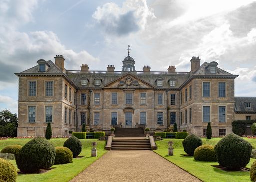 A beautifully landscaped formal garden surrounds the grand front entrance of an ancient house