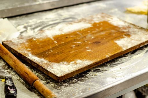 A closeup shot of flour on a wooden chopping board with a rolling pin and knife on a kitchen