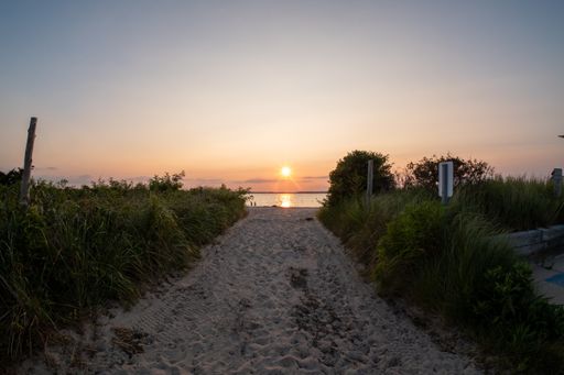 A picturesque pathway meanders through a lush green landscape, leading to the tranquil waters of a pristine beach
