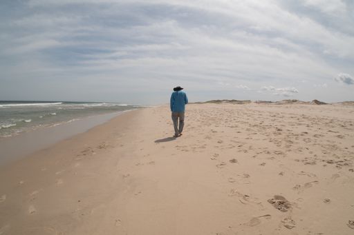 A male individual strolls along the sandy beach, heading towards the serene ocean in search of solace and tranquility