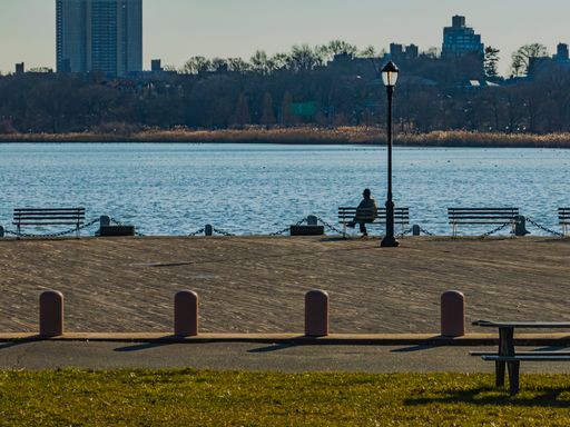 A group of individuals are seated on wooden benches in a park, enjoying the serene view of the water