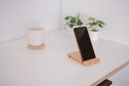 A closeup shot of a white cup and a phone on a wooden board