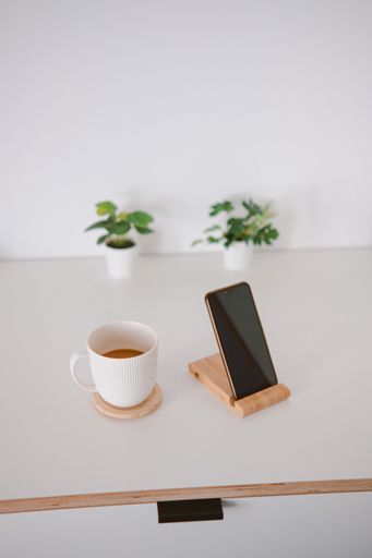 A vertical shot of a white cup and a phone on a wooden board