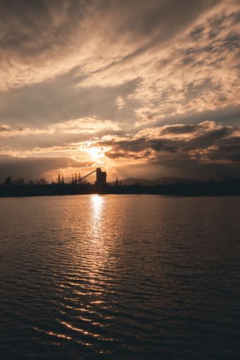A vertical shot of the lake with a city in the background under a cloudy sunset sky