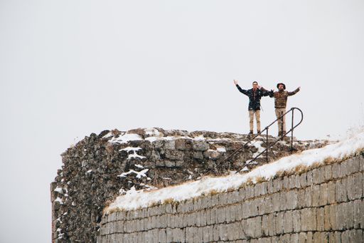 Two adult hikers standing on an abandoned building covered in the snow in Brignogan, France