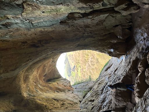 Two individuals explore a dimly lit underground cave, their silhouettes illuminated by the faint glow of natural light filtering through a distant opening