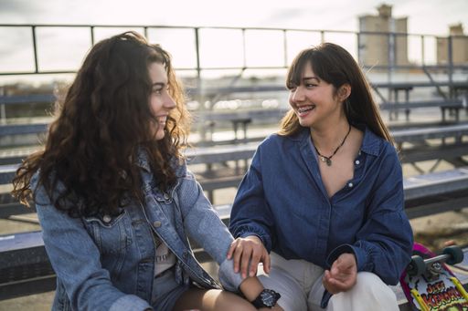 Two girls sitting and talking to each other behind a metal fence during daytime