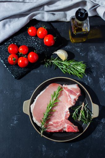 A vertical shot of a pork steak with cherry tomatoes, rosemary, garlic, and olive oil on a table