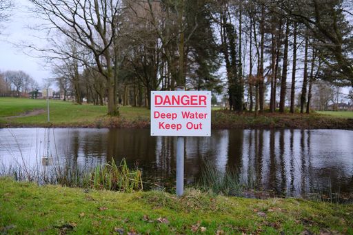 danger deep water warning sign by a water filled pond risk to the public of drowning