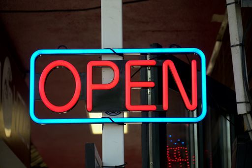 A closeup shot of an illuminated neon light sign with red open text on the steel post