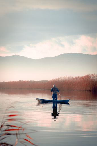 A man fishing in the misty river, capturing fish with a net from the boat