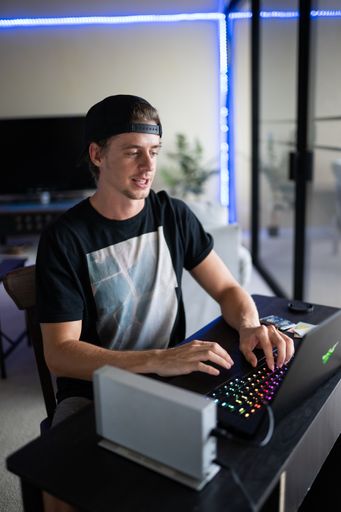 A vertical shot of a young American dude gaming on his ultrapowerful laptop in his house