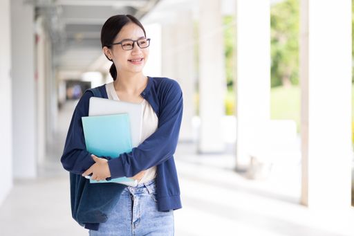 A happy young Asian student holding books while strolling around on campus