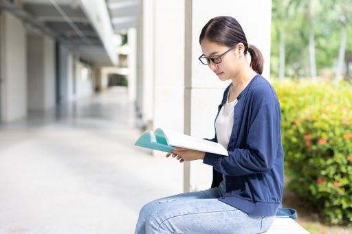 A young smart woman sitting reading a book on university campus
