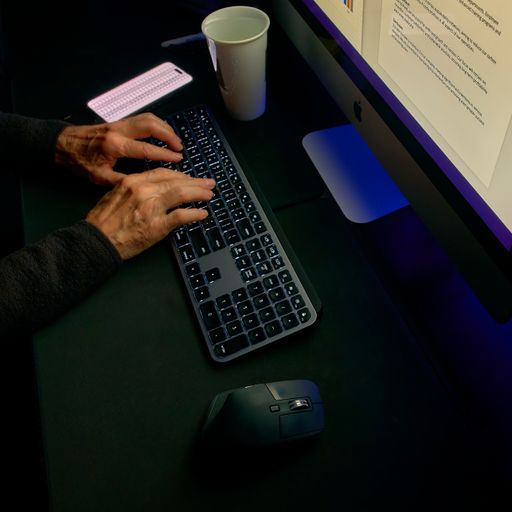 Close-up of hands typing on a keyboard and using a mouse in a darkened room, denoting focused work.