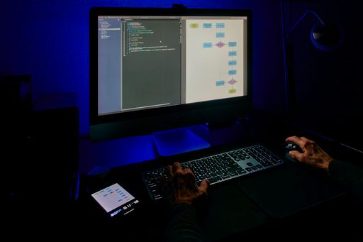 An experienced programmer is engaged in software development using a dual-window, a coding interface in one window and a flowchart design in the other