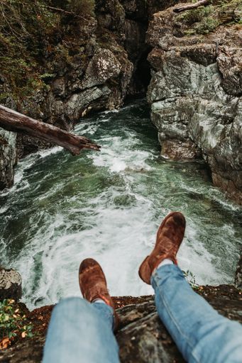 A man sitting on top of a rocky mountain and enjoying the view of a river