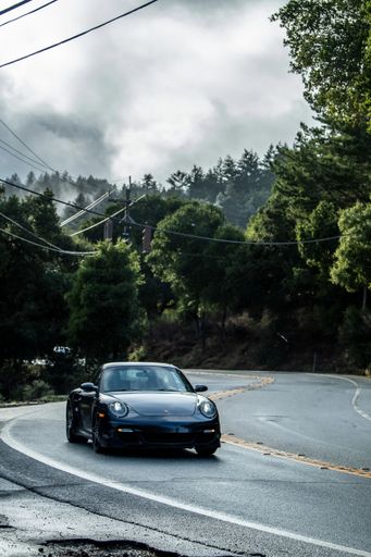 A Modern Porsche car coming down a winding road on a cloudy day with misty forest in the background