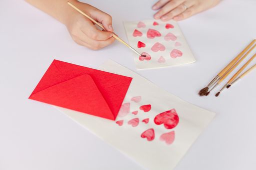 A closeup of a person crafting paper hearts with pencils on an envelope for Valentine's day
