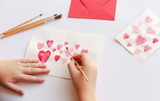 A closeup of a person crafting paper hearts with pencils on an envelope for Valentine's day