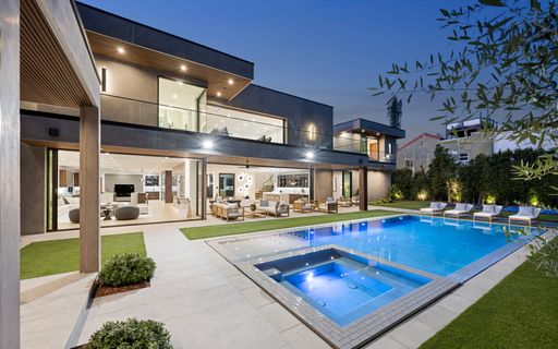 An evening view of an outdoor pool located on a deck adjacent to a house, New Construction Home in Tarzana, California